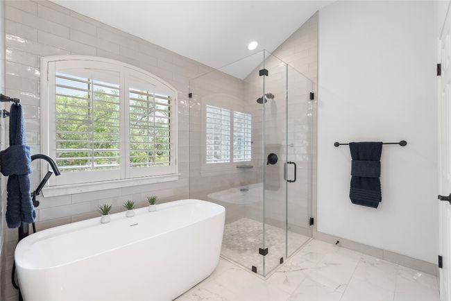 Stylish primary bath featuring a freestanding soaking tub, frameless glass shower, plantation shutters, and sleek finishes throughout. | Image 28