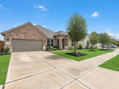 This is a single-story, brick home with a two-car garage and a well-manicured lawn featuring young trees and shrubs. The neighborhood appears to be a suburban setting with open skies. | Image 3