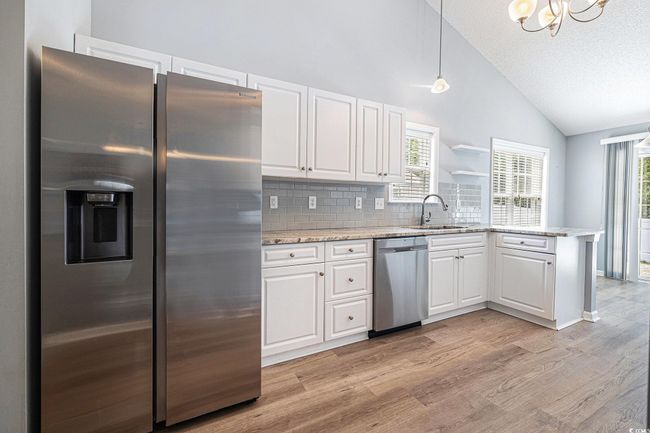 Kitchen featuring appliances with stainless steel finishes, light wood-style floors, white cabinetry, a peninsula, and backsplash | Image 14