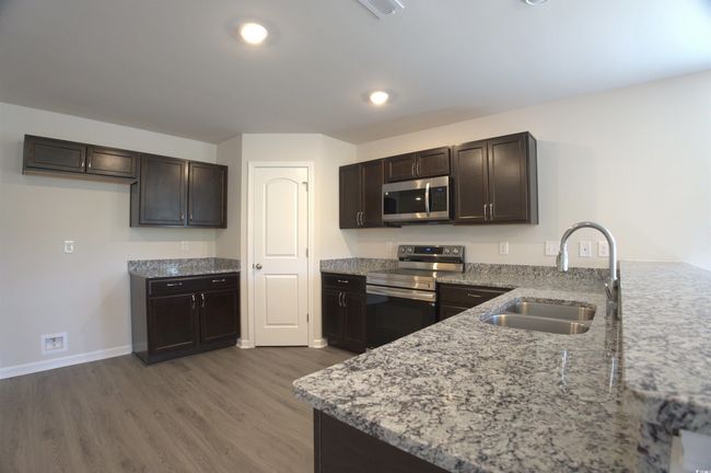 Kitchen with appliances with stainless steel finishes, light stone counters, wood finished floors, dark brown cabinetry, and a peninsula | Image 8
