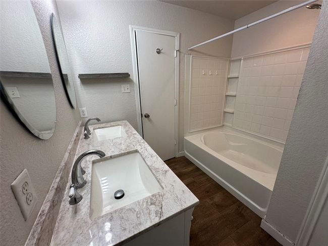 Bathroom with a textured wall, wood finished floors, shower combination, and double vanity | Image 35