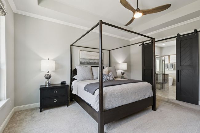 Bedroom featuring a barn door, light colored carpet, ornamental molding, ensuite bath, and a ceiling fan | Image 17