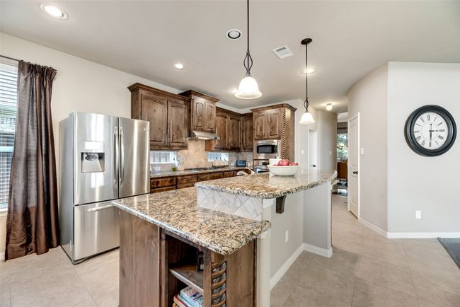 Kitchen featuring appliances with stainless steel finishes, under cabinet range hood, open shelves, light stone countertops, and a kitchen island with sink | Image 5