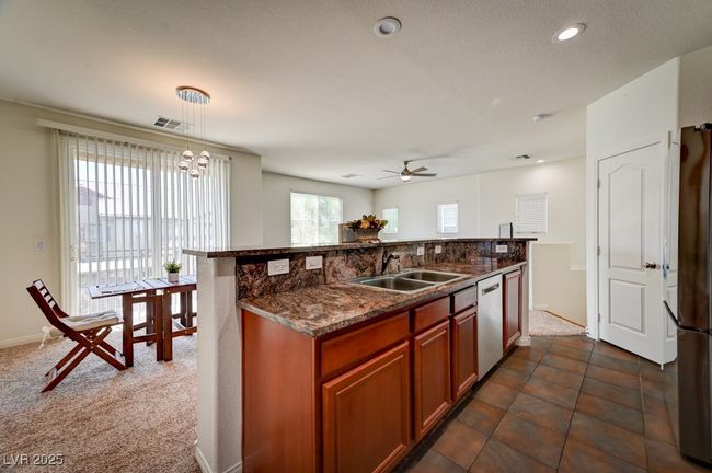 Kitchen with hanging light fixtures, freestanding refrigerator, brown cabinetry, ceiling fan, and stainless steel dishwasher | Image 11