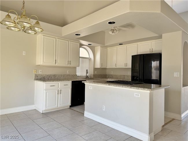 Kitchen with a kitchen island, a tray ceiling, an inviting chandelier, white cabinets, and black appliances | Image 7
