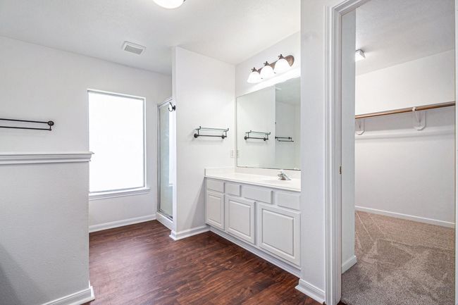 Bright primary bathroom with vinyl wood-style flooring, featuring a large mirror and a sleek vanity. Includes a shower, soaking tub and large walk-in closet space accessible through an open doorway. | Image 9