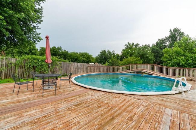 View of pool with a wooden deck, a fenced backyard, and view of scattered trees | Image 36