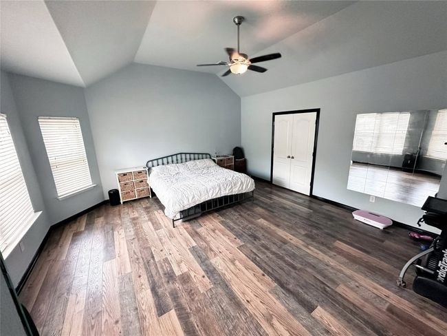 Large primary bedroom on first floor featuring vaulted ceiling, wood finished floors, and ceiling fan showing mirrored wall | Image 15