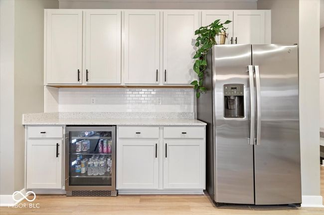 kitchen featuring stainless steel refrigerator with ice dispenser, wine cooler, white cabinetry, and light stone counters | Image 19
