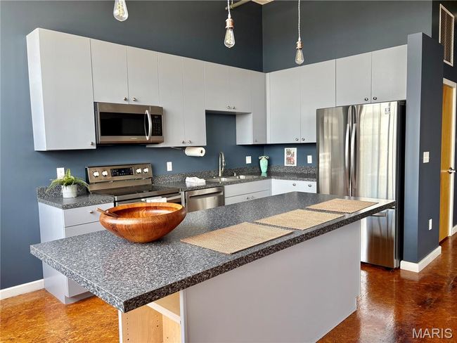 Kitchen with freestanding refrigerator, dark countertops, open floor plan, white cabinets, and finished concrete floors | Image 18