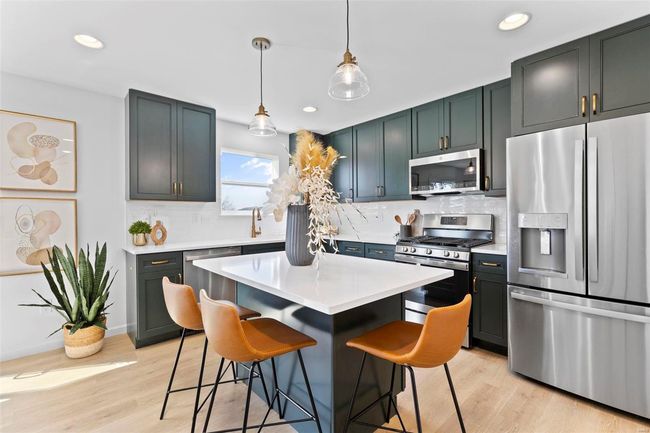 Kitchen featuring appliances with stainless steel finishes, hanging light fixtures, light wood-type flooring, and a breakfast bar area | Image 15