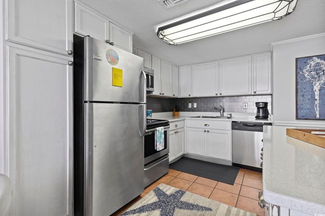 Kitchen with light tile patterned flooring, white cabinets, a sink, and appliances with stainless steel finishes | Image 18