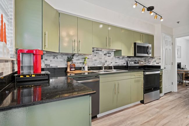 The kitchen features sage cabinetry, granite countertops, a mosaic tile backsplash, and stainless appliances | Image 7