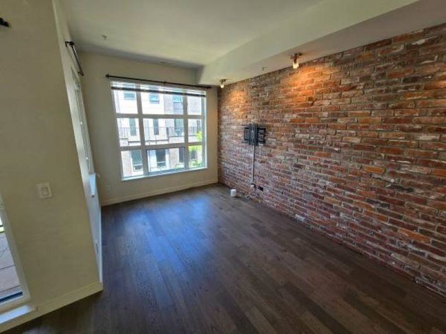 Empty room with baseboards, dark wood-type flooring, and brick wall | Image 8