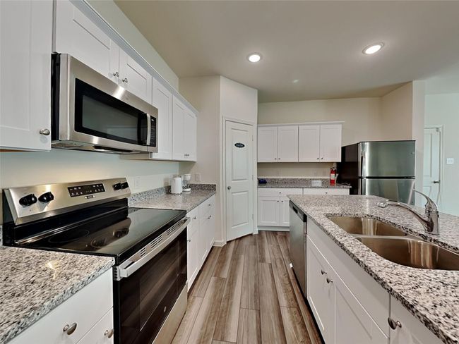 Kitchen featuring appliances with stainless steel finishes, light wood finished floors, white cabinets, recessed lighting, and light stone counters | Image 9