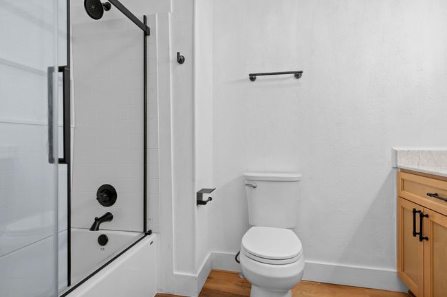 Bathroom featuring shower / bath combination with glass door, vanity, baseboards, toilet, and wood finished floors | Image 27