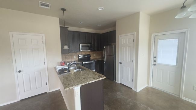 Kitchen with stainless steel appliances, concrete floors, backsplash, light stone countertops, and decorative light fixtures | Image 4