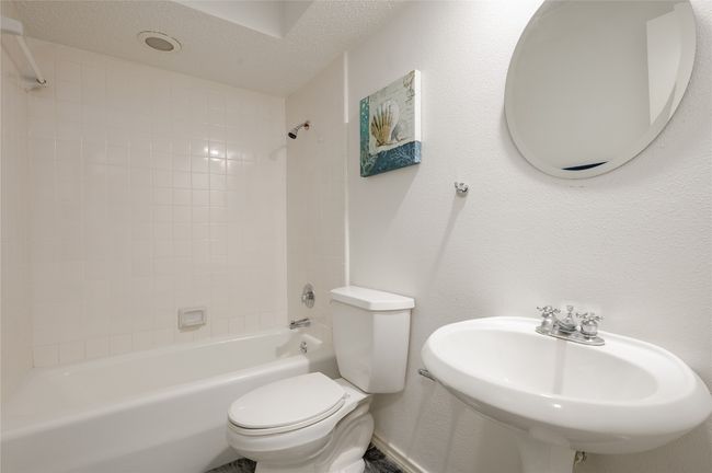 Bathroom with a textured wall, shower / bathing tub combination, toilet, a sink, and a textured ceiling | Image 23