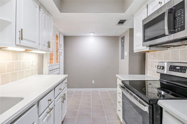 Kitchen featuring stainless steel appliances, white cabinets, light countertops, decorative backsplash, and baseboards | Image 15
