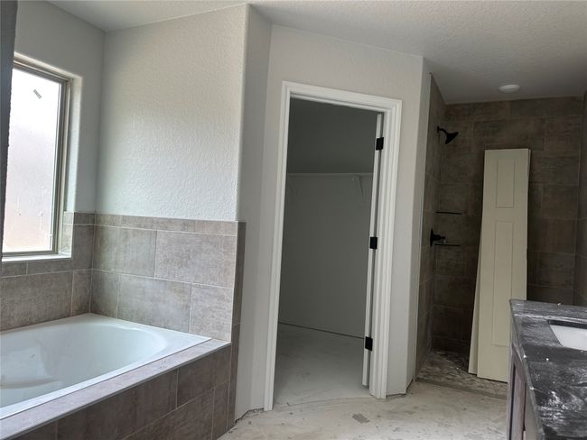 Full bathroom featuring a garden tub, tiled shower, a walk in closet, a textured ceiling, and vanity | Image 13