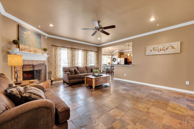 Living room with a ceiling fan, ornamental molding, stone tile flooring, recessed lighting, and a fireplace with raised hearth | Image 6