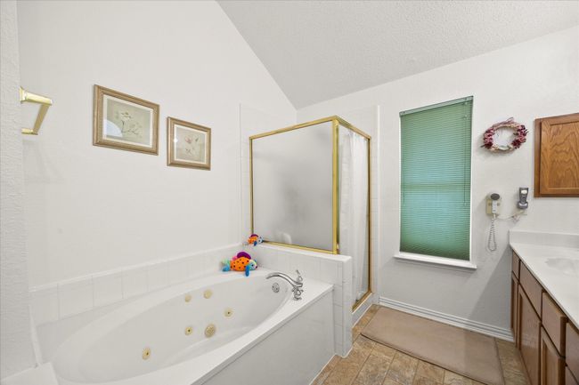 Bathroom with a jetted tub, a shower stall, vanity, vaulted ceiling, and a textured ceiling | Image 13