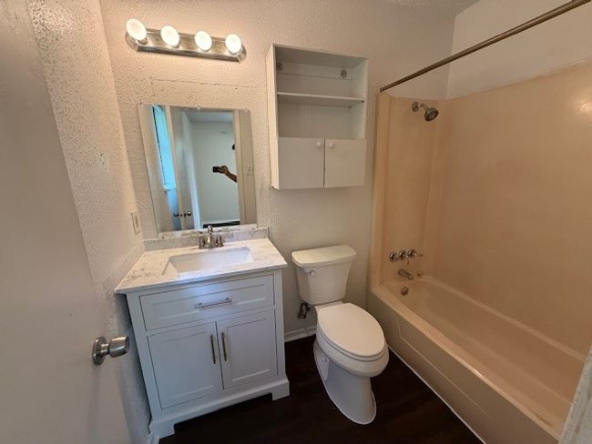 Full bathroom featuring wood finished floors, shower / tub combination, vanity, and a textured wall | Image 10