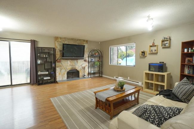 Living area featuring a baseboard radiator, a textured ceiling, wood finished floors, and a fireplace | Image 8