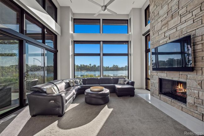 Living area with carpet floors, a stone fireplace, a towering ceiling, ceiling fan, and healthy amount of natural light | Image 15
