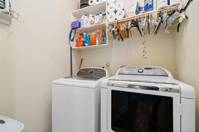 This laundry room features a washer and dryer set, overhead shelving for storage, and a hanging rod for clothes. The space is compact yet efficiently organized. | Image 39