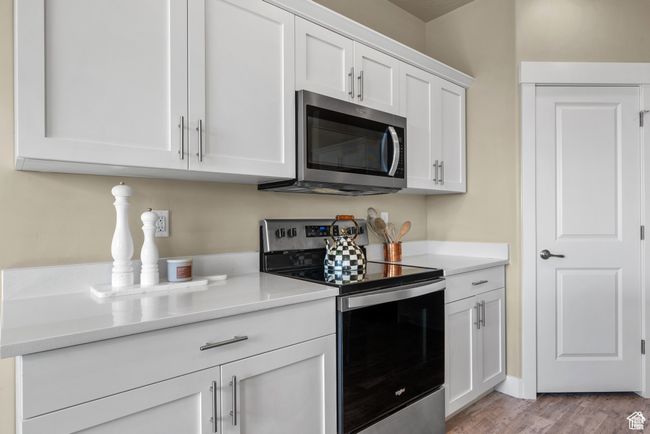 Kitchen with light wood-type flooring, light countertops, white cabinetry, and stainless steel appliances | Image 11