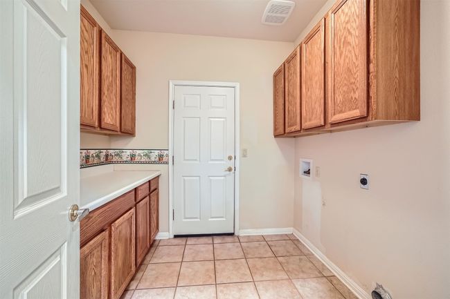 Laundry area featuring cabinet space, washer hookup, hookup for an electric dryer, light tile patterned floors, and baseboards | Image 22
