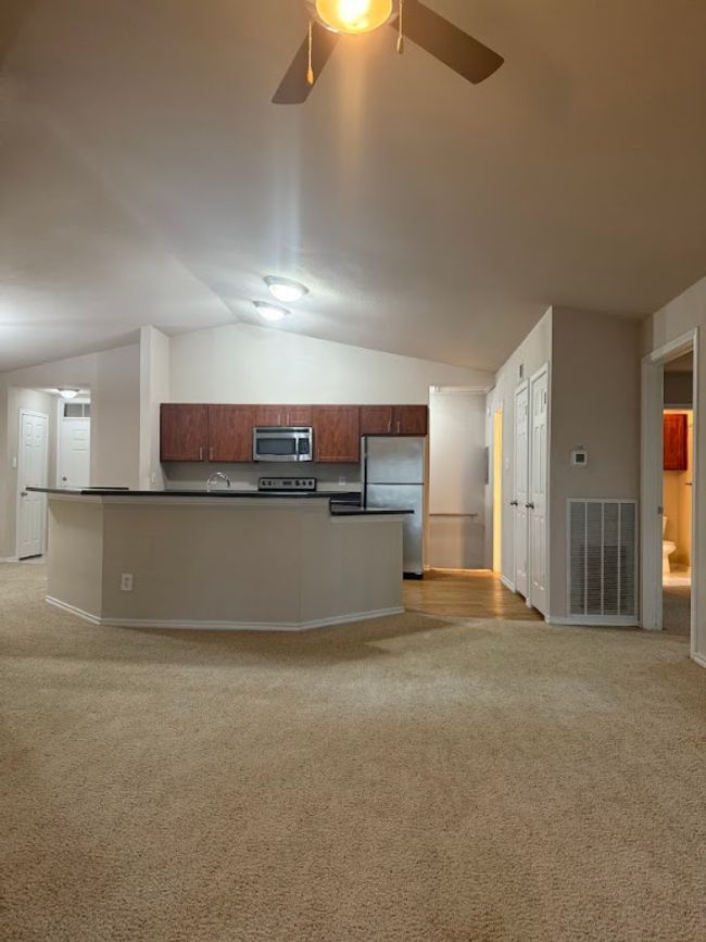 Kitchen with appliances with stainless steel finishes, dark countertops, vaulted ceiling, light carpet, and a ceiling fan | Image 4