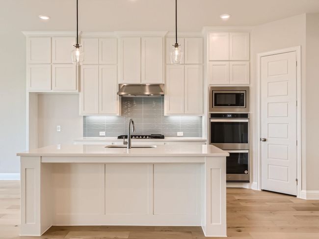 Kitchen featuring tasteful backsplash, light countertops, appliances with stainless steel finishes, under cabinet range hood, and white cabinetry | Image 9