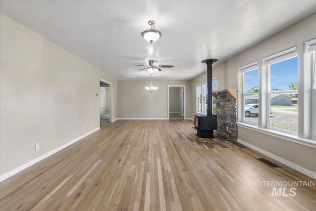 Unfurnished living room with a wood stove, light wood-style floors, ceiling fan, and a chandelier | Image 12