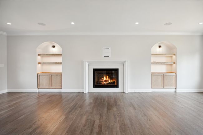 Unfurnished living room featuring built in features, crown molding, a glass covered fireplace, wood finished floors, and recessed lighting | Image 4