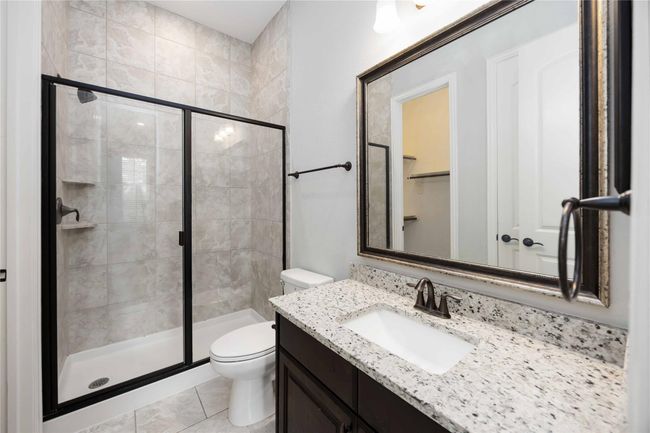 This bathroom features a sleek design with a tiled walk-in shower, glass door, and a modern vanity with a granite countertop. It has a large framed mirror and contemporary fixtures, offering a clean and stylish look. | Image 37