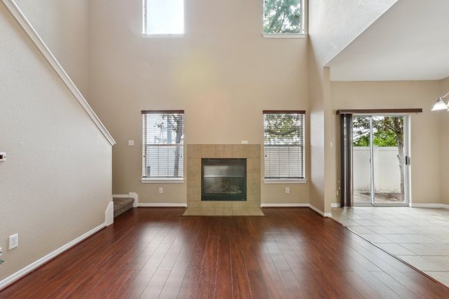 Unfurnished living room featuring a towering ceiling, a tiled fireplace, baseboards, and wood-type flooring | Image 6