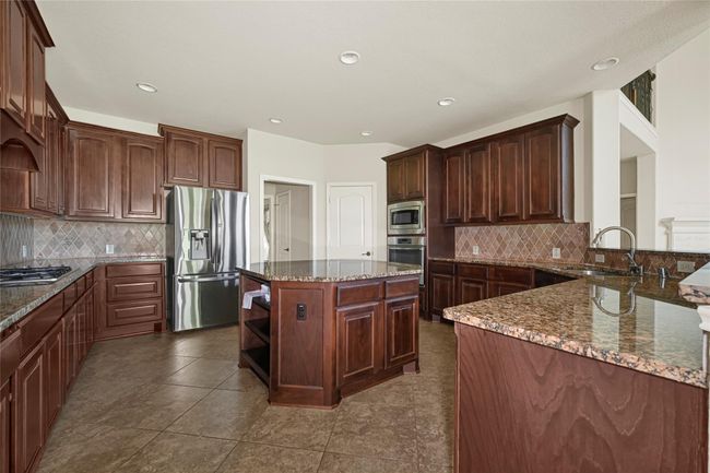 A generous kitchen awaits, with dark wood cabinetry, granite countertops, and a central island. The extended raised bar adds both style and function while subtly defining the space. | Image 16