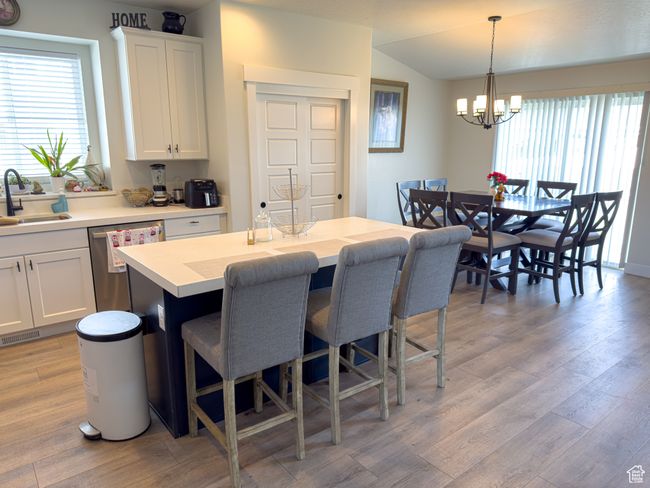Kitchen with dishwasher, a breakfast bar, a chandelier, light wood-type flooring, and white cabinets | Image 9