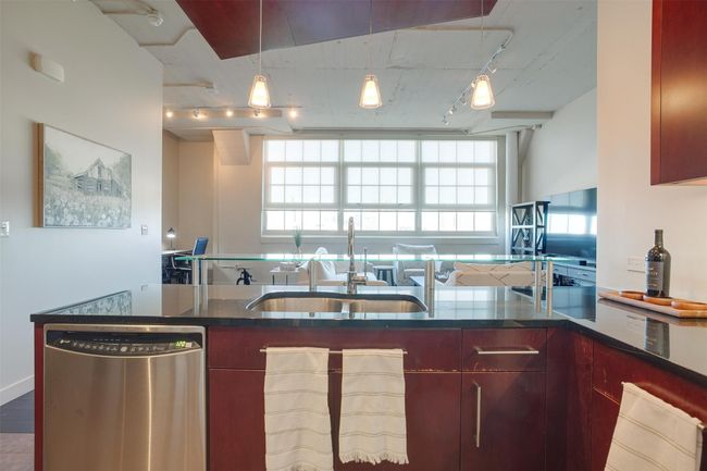 Kitchen with dishwasher, track lighting, decorative light fixtures, dark stone countertops, and reddish brown cabinets | Image 14