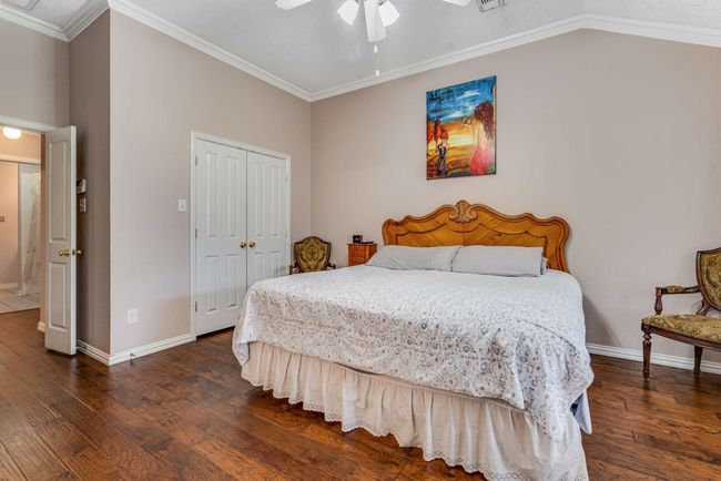 Bedroom with hardwood finished floors, baseboards, a walk-in closet, ornamental crown molding, and a ceiling fan | Image 23