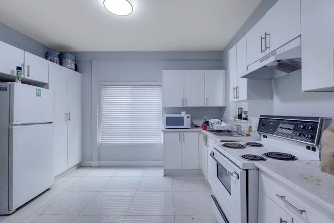 Kitchen featuring white cabinets, light tile patterned flooring, white appliances, and under cabinet range hood | Image 31