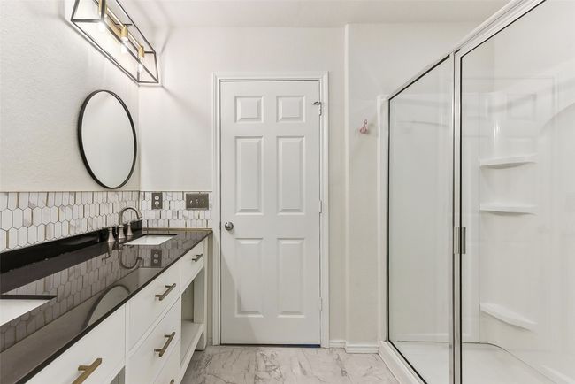 Full bathroom featuring double vanity, a stall shower, backsplash, marble finish floor, and a sink | Image 19
