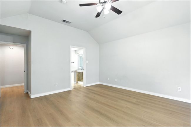 Unfurnished bedroom with vaulted ceiling, wood finished floors, connected bathroom, and a ceiling fan | Image 28