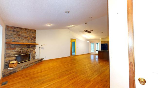 Unfurnished living room with visible vents, light wood-style flooring, ceiling fan, a stone fireplace, and vaulted ceiling | Image 4