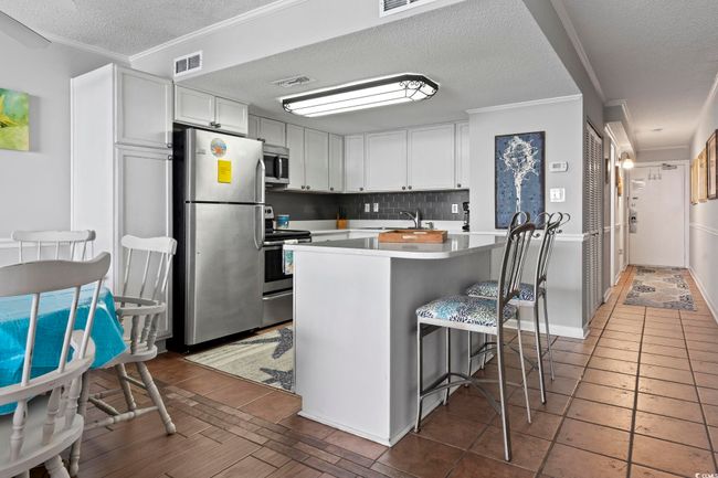 Kitchen with light countertops, visible vents, crown molding, a breakfast bar, and stainless steel appliances | Image 19
