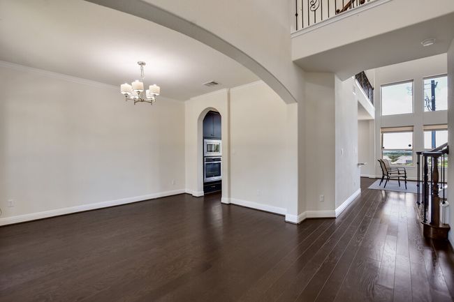 Empty room with a chandelier, arched walkways, ornamental molding, dark wood-style flooring, and a towering ceiling | Image 7
