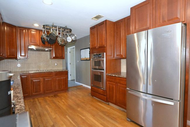 Kitchen featuring light wood finished floors, brown cabinets, under cabinet range hood, stainless steel appliances, and visible vents | Image 4