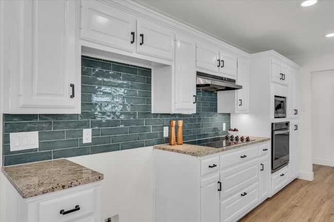 Kitchen featuring black electric cooktop, under cabinet range hood, white cabinetry, stainless steel oven, and light stone counters | Image 21
